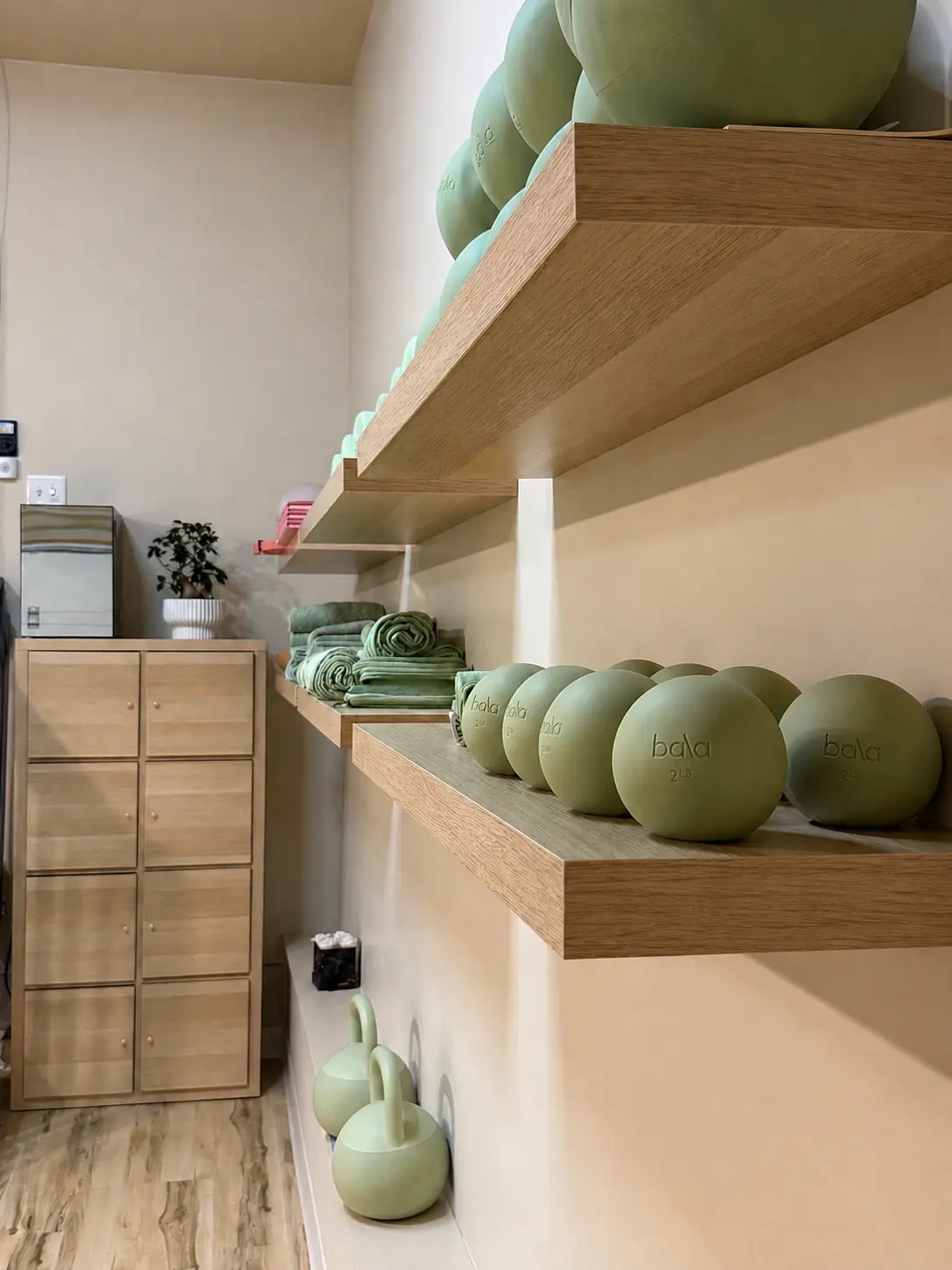 Wooden studio shelves holding mint-green exercise balls, rolled towels and kettlebells